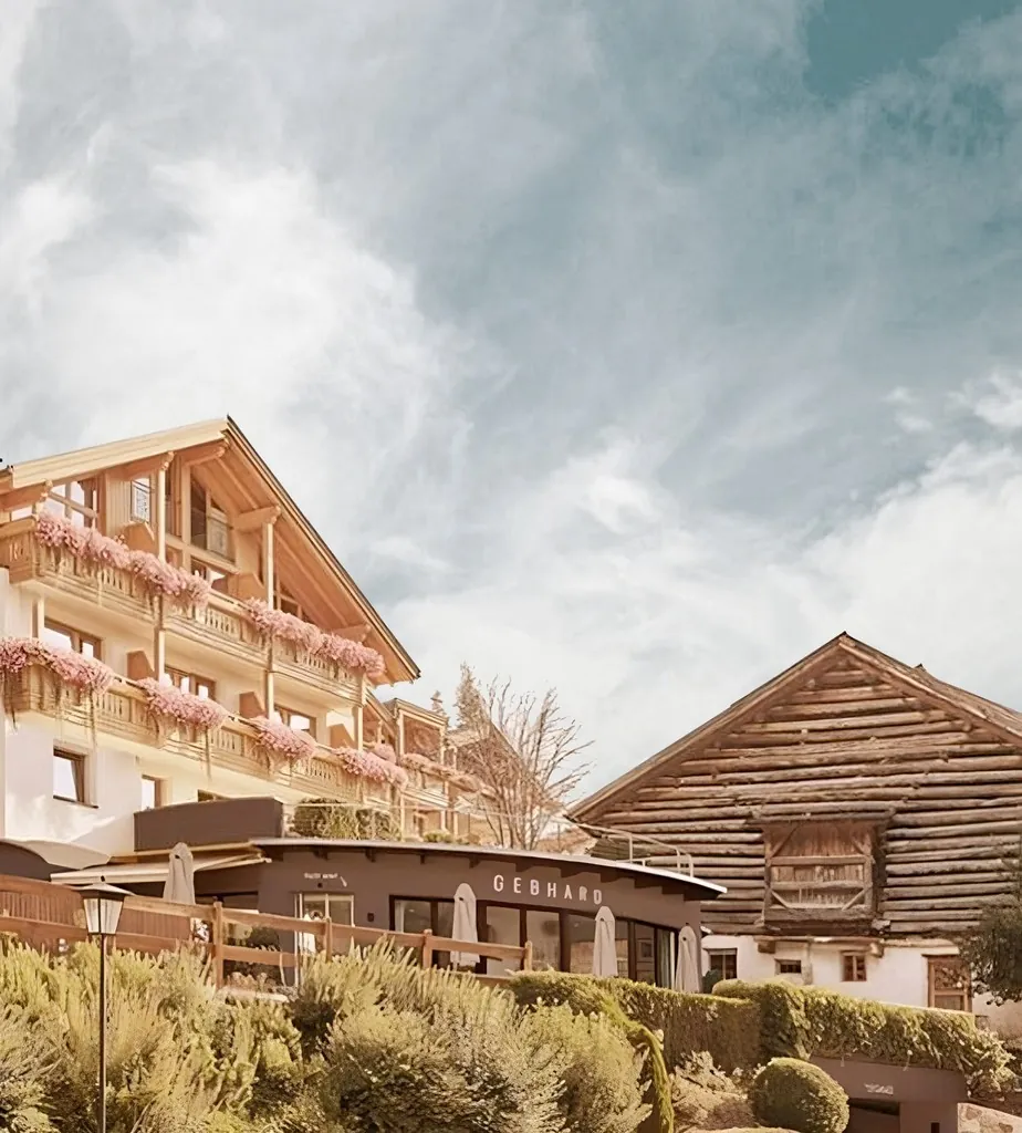 Hotelfassade mit Holzbalkonen, blühenden Blumenkästen und Bergblick im Hintergrund