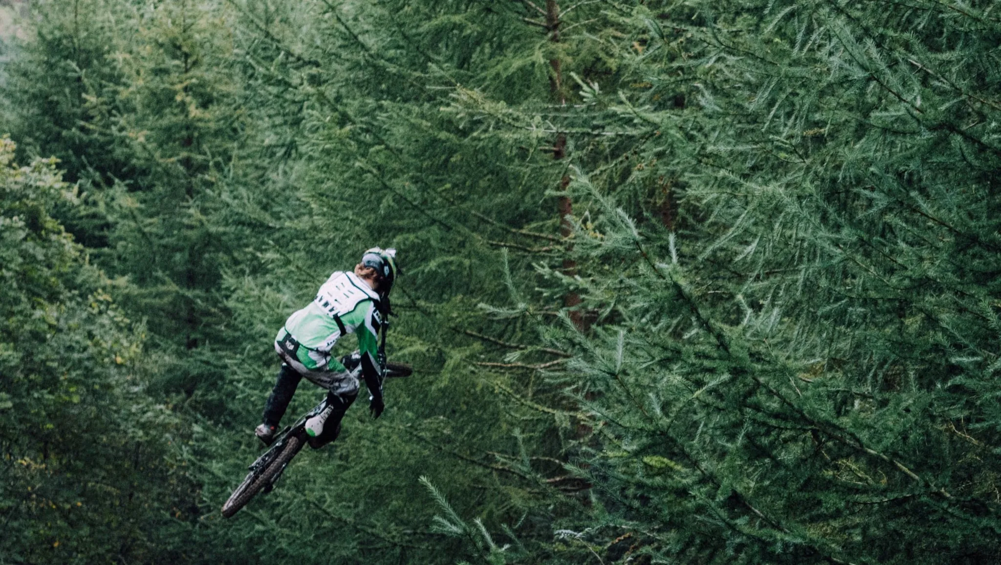 Mountainbiker im Sprung hoch über einem dichten Nadelwald