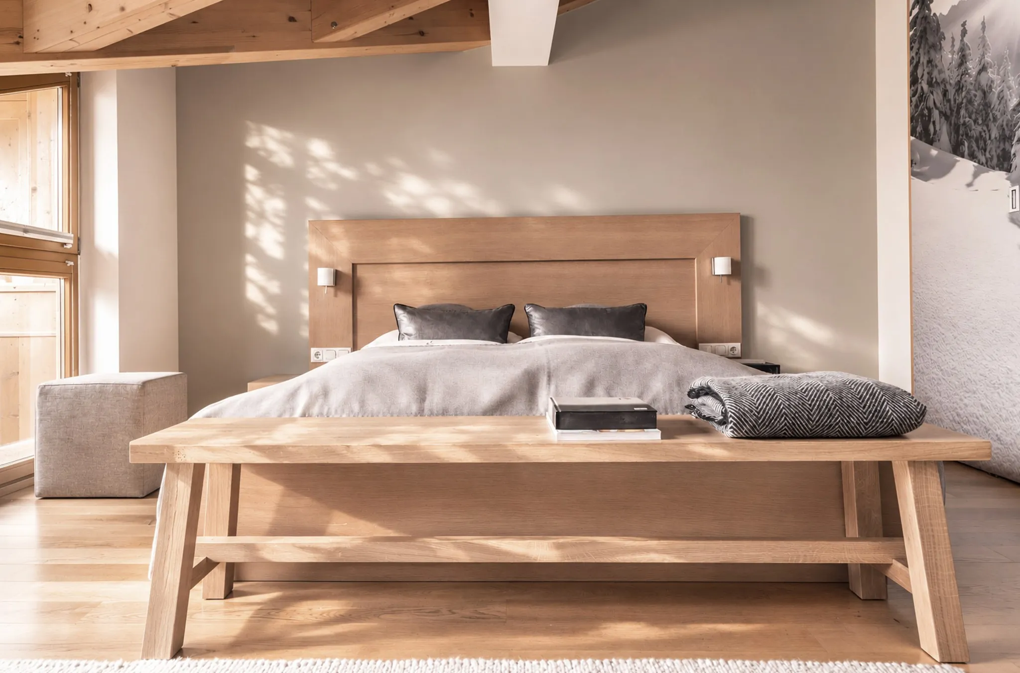 Helles Hotelzimmer mit Holzbett, Sitzbank und Sonnenlicht am Fenster