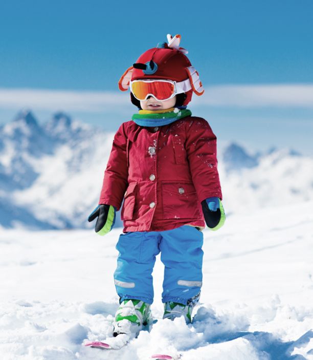 Kleines Kind in roter Jacke steht allein auf Ski im Schnee, dahinter die Bergkette