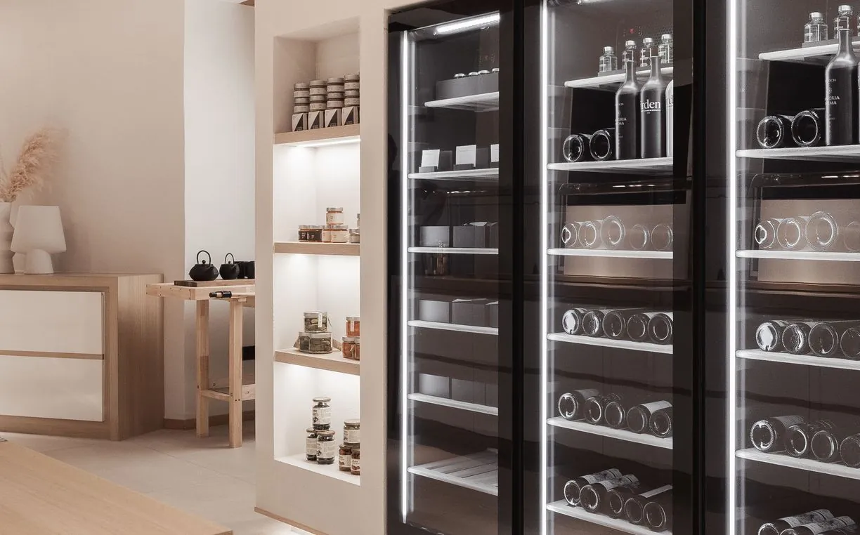 Regal mit regionalen Produkten in Gläsern, daneben die beleuchteten Weinkühlschränke