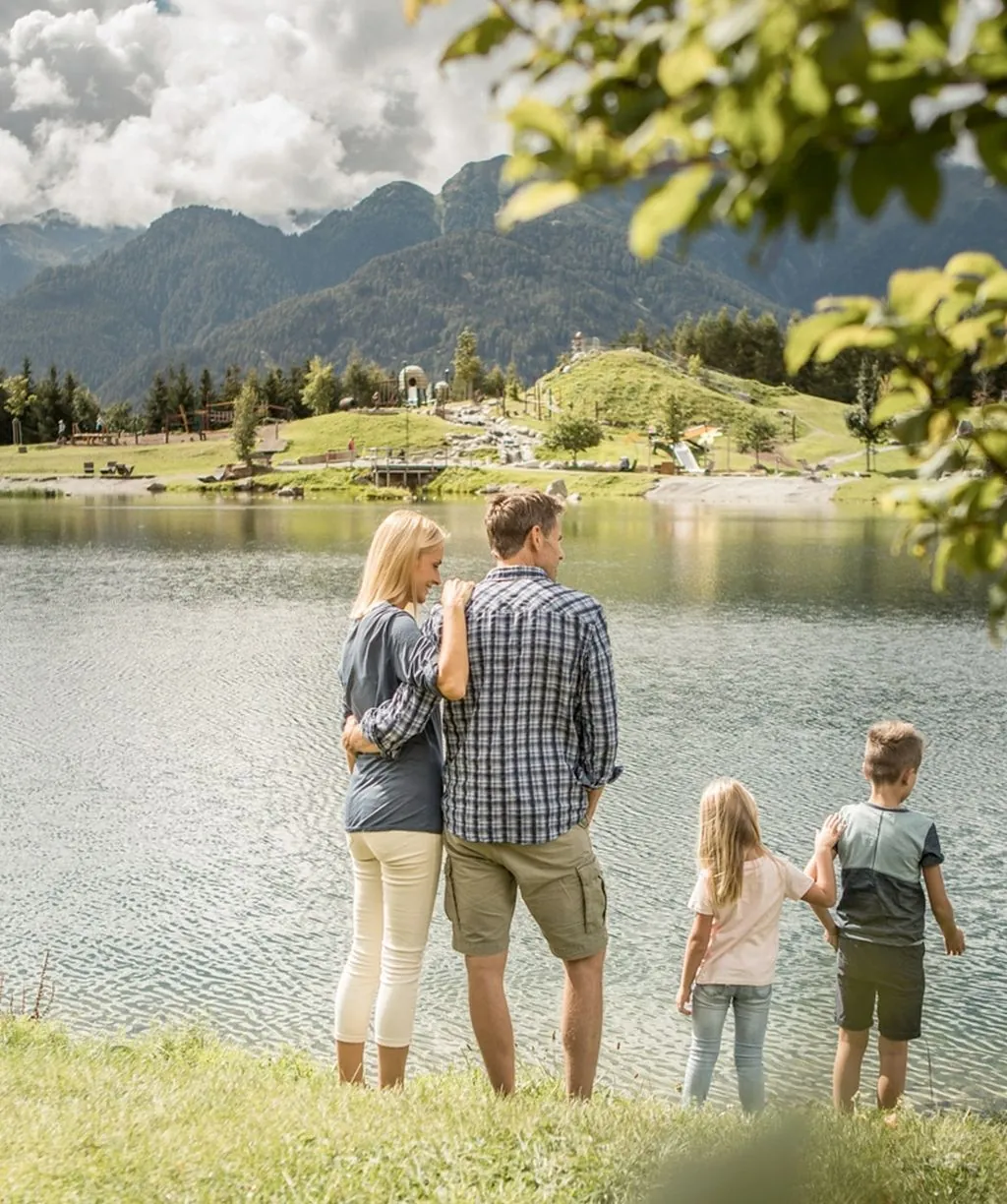 Eltern mit zwei Kindern stehen am Ufer eines Bergsees