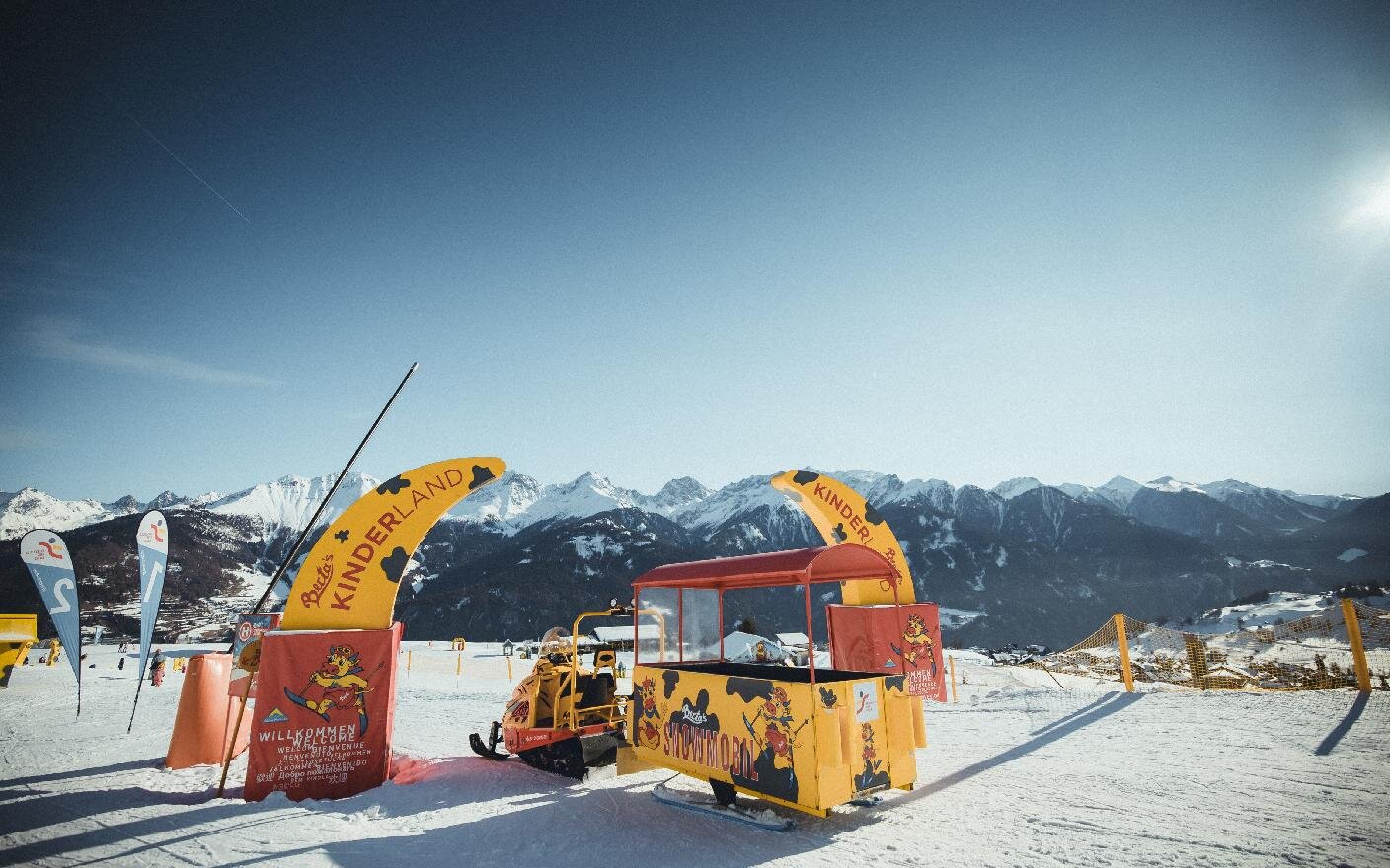 Die Maskottchen Berta und Bertl stehen vor einer Pistenraupe im Schnee