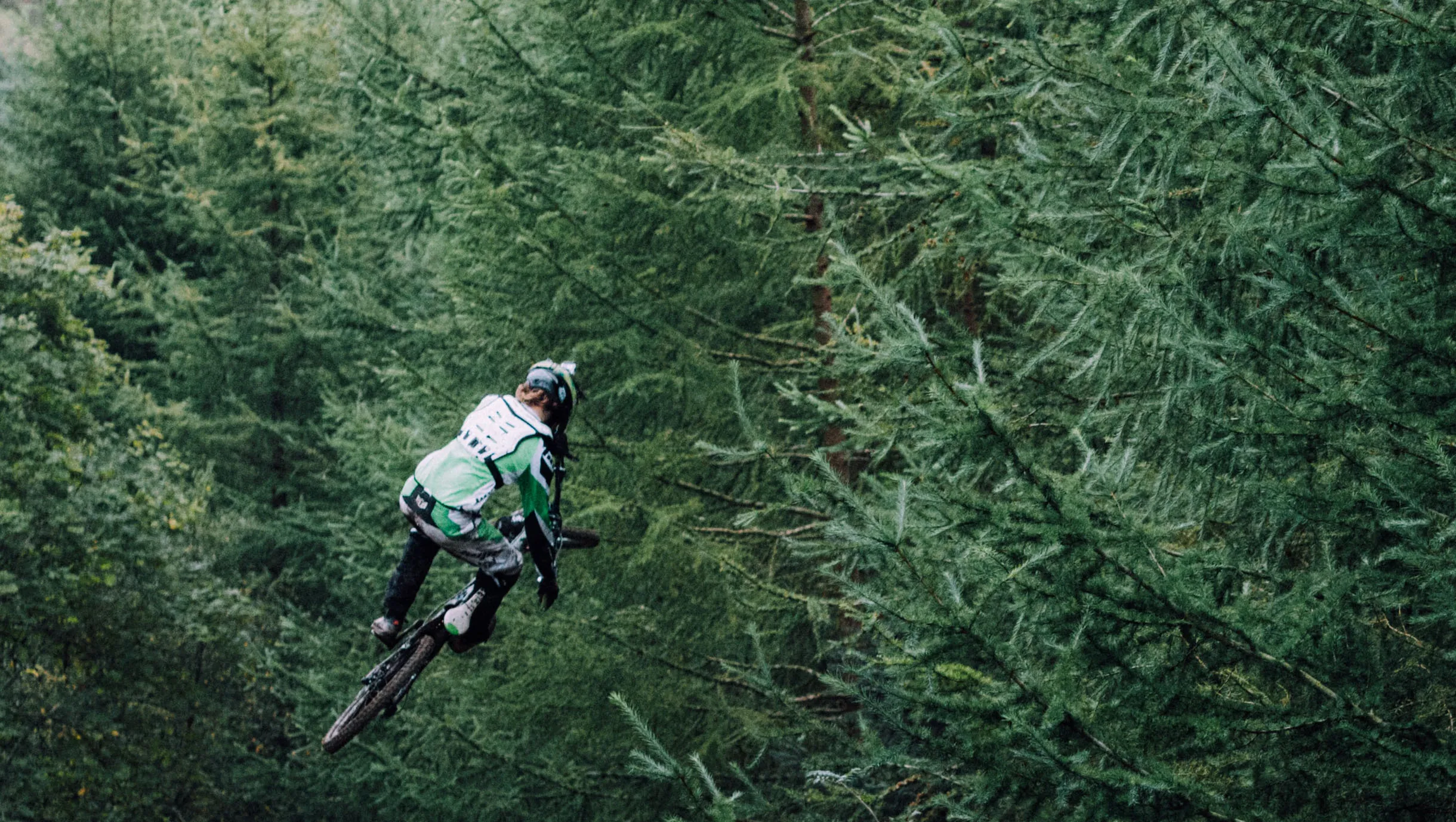 Mountainbiker von oben gesehen als kleine Figur auf einem Trail im dichten Nadelwald.