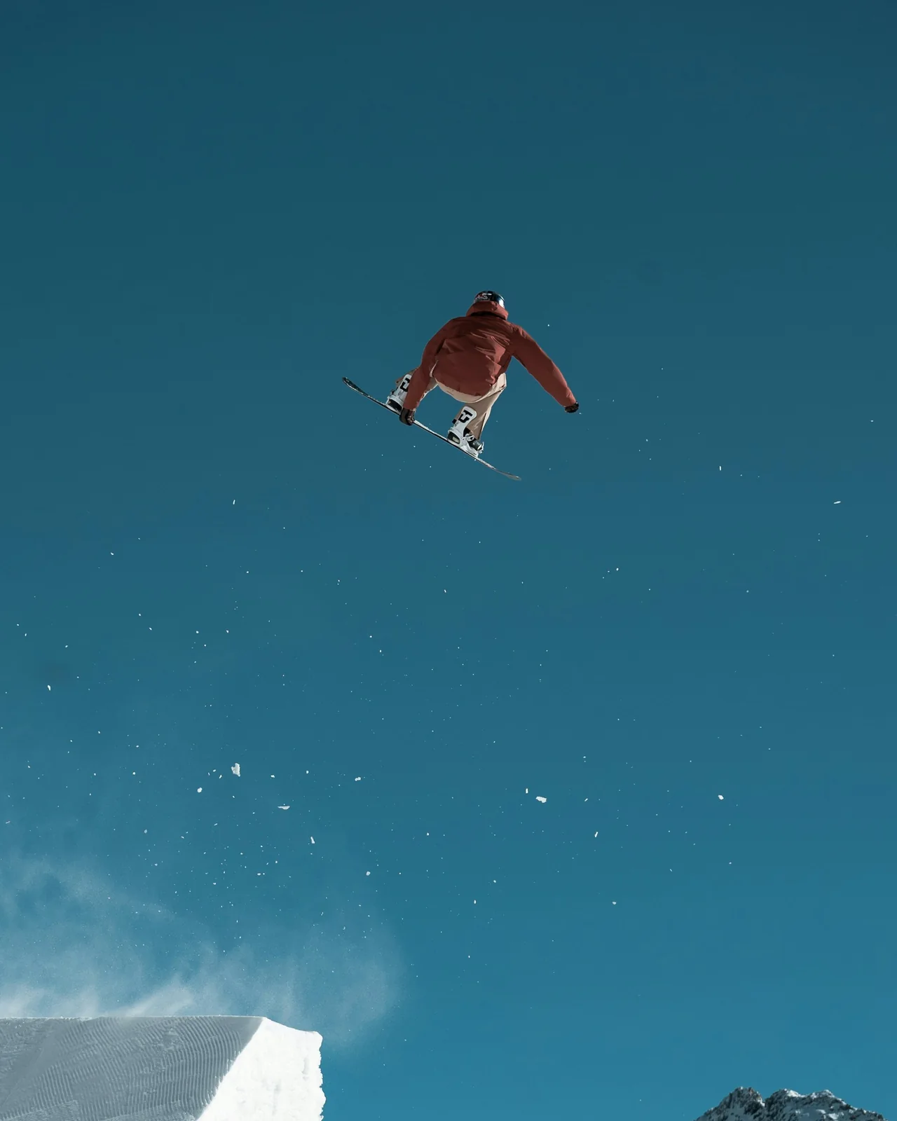 Snowboarder springt über einen Kicker im Funpark, dahinter die Gipfel