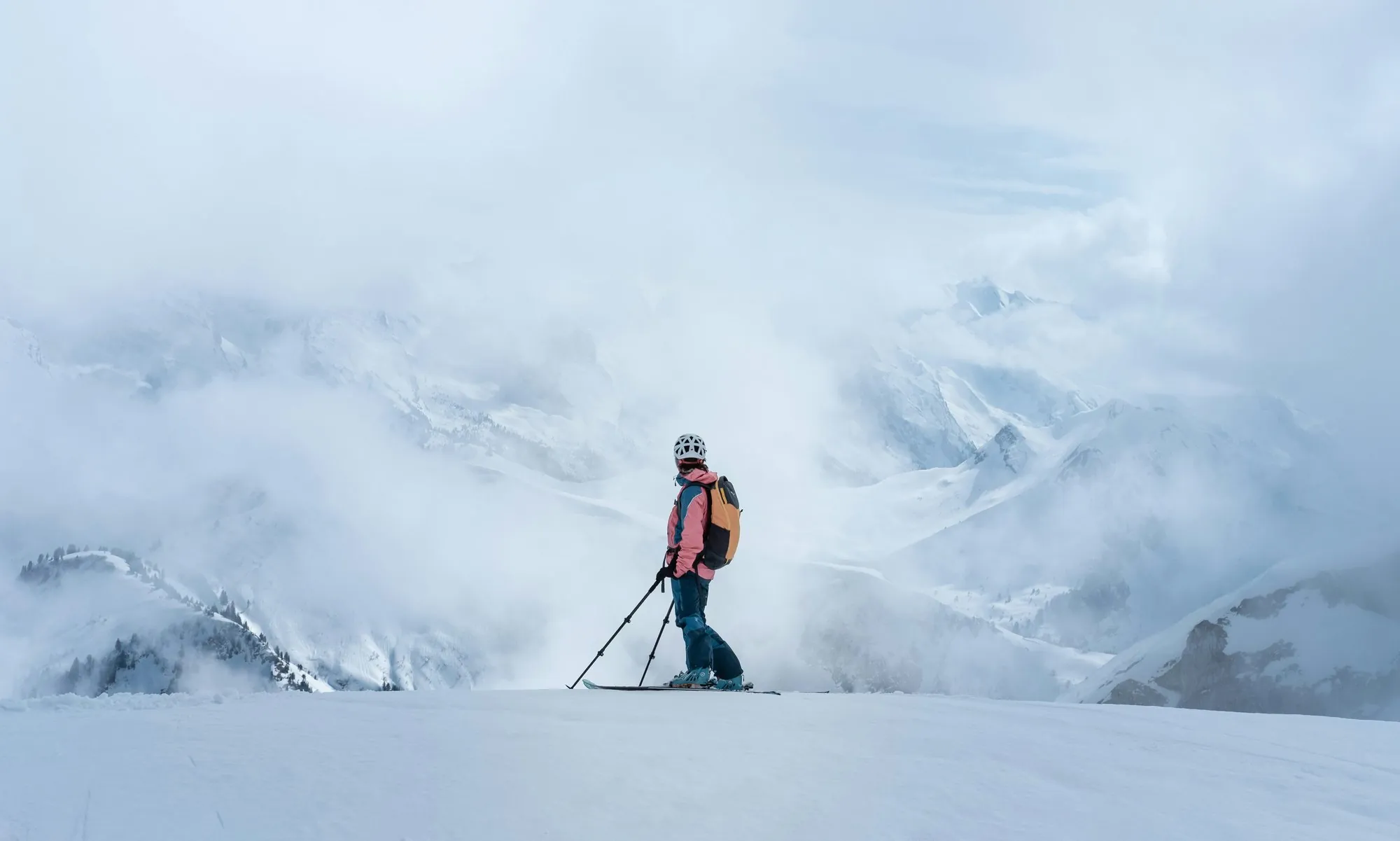 Skifahrerin steht am Grat und blickt über ein Wolkenmeer zwischen den Gipfeln
