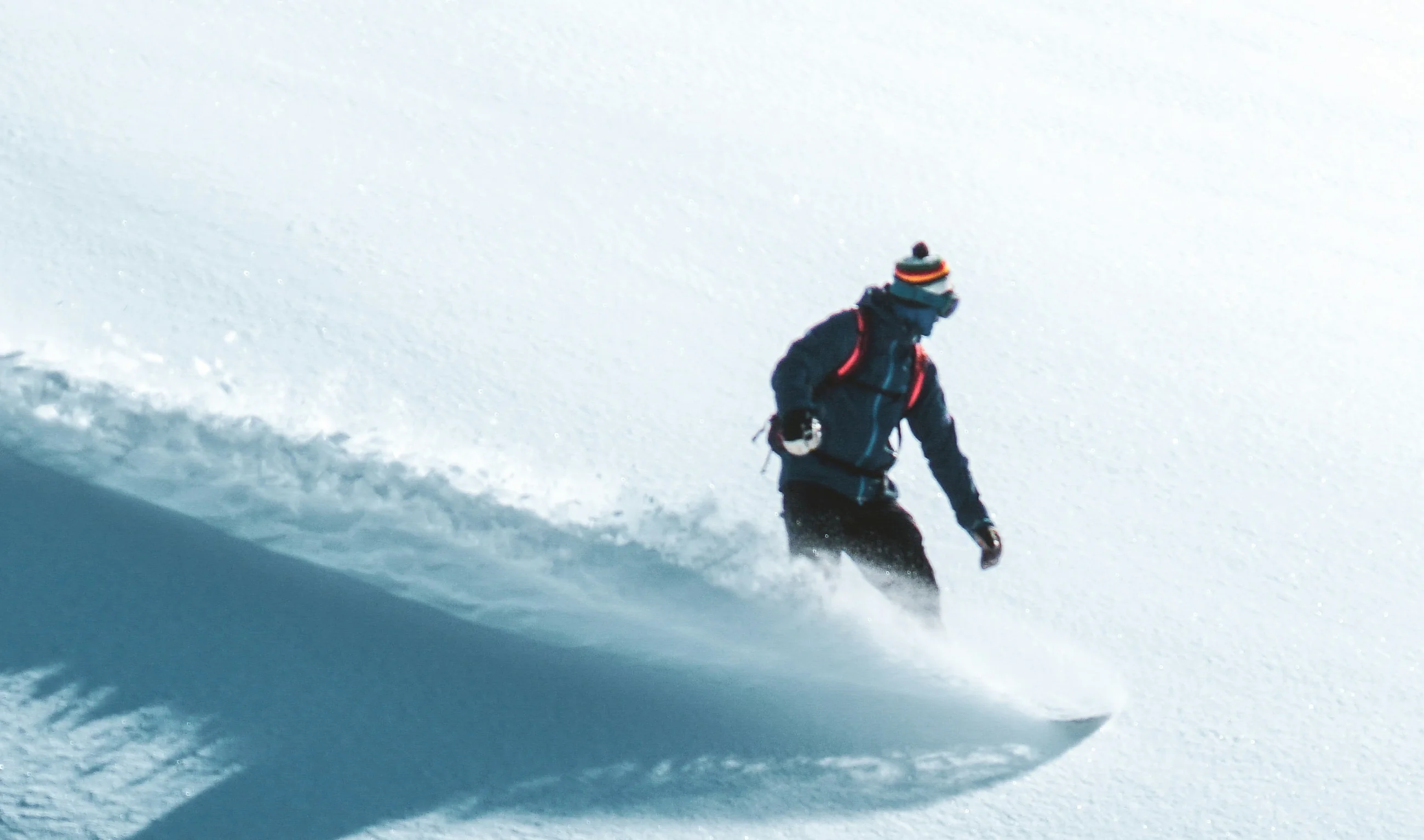 Snowboarder zieht eine Welle aus Pulverschnee hinter sich her