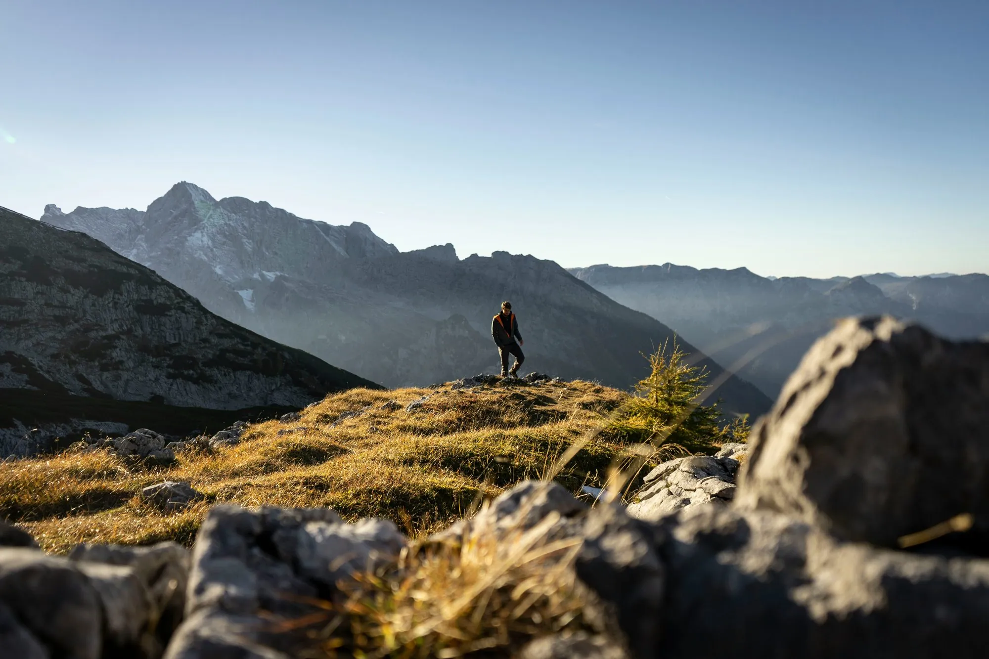 Wanderer auf einem Bergrücken im Gegenlicht, dahinter die Bergkette im Dunst