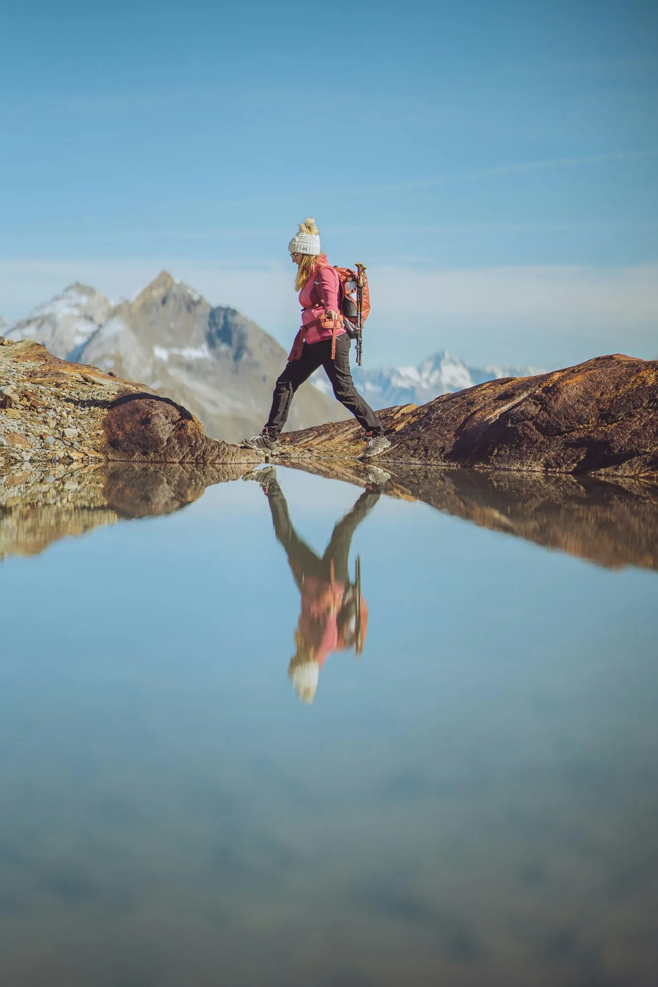 Wanderin auf einem Felsen am Bergsee, ihre Spiegelung im stillen Wasser