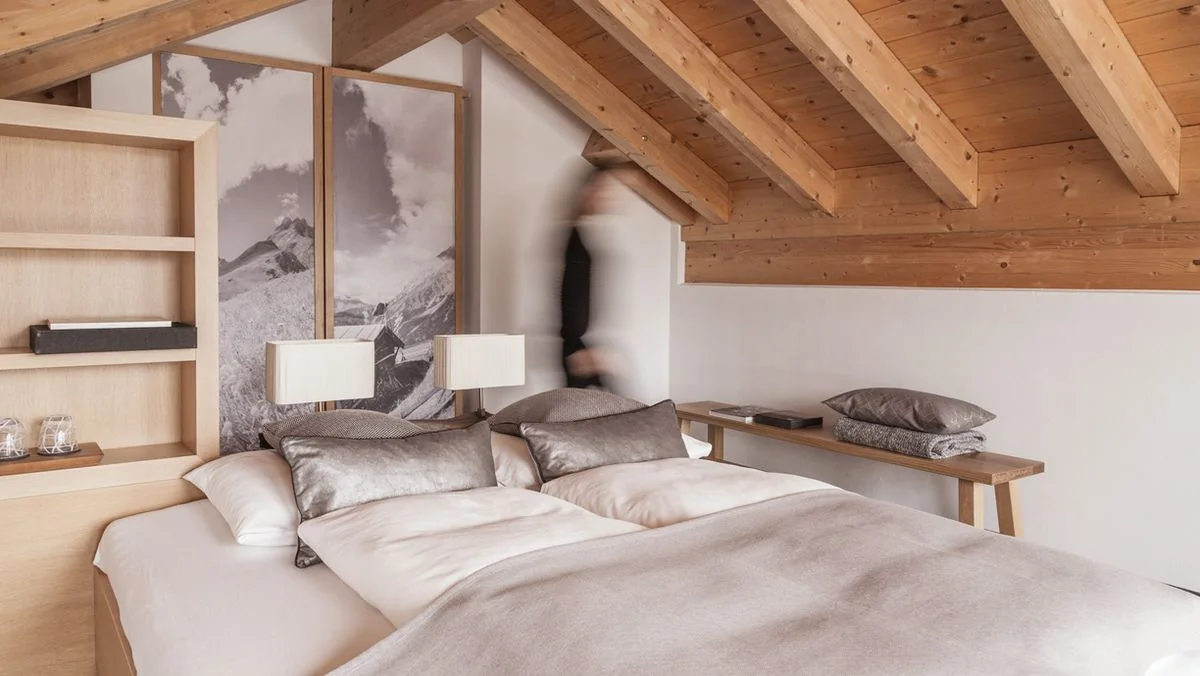 Bett unter den Holzbalken der Dachschräge, daneben der Aufgang