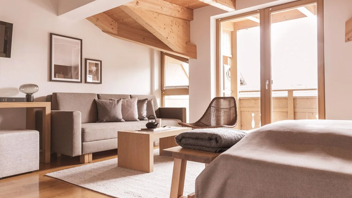 Dachzimmer mit sichtbaren Holzbalken, Sofa und Tisch am Fenster